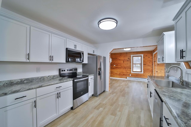 kitchen featuring light wood-style floors, wooden walls, baseboard heating, a sink, and appliances with stainless steel finishes