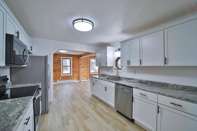 kitchen with baseboard heating, a sink, wooden walls, stainless steel appliances, and light wood-style flooring