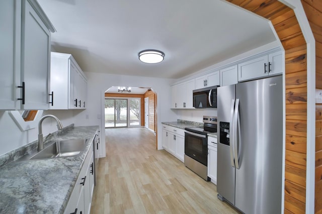 kitchen featuring appliances with stainless steel finishes, a sink, arched walkways, white cabinetry, and light wood-type flooring