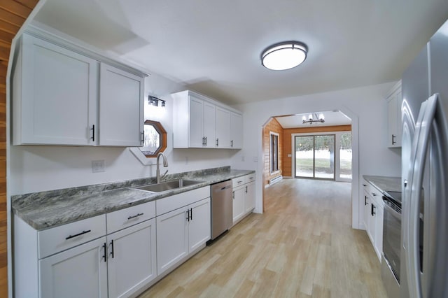 kitchen with an inviting chandelier, a sink, light wood-style floors, arched walkways, and stainless steel appliances
