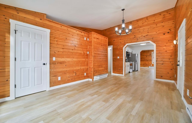 unfurnished dining area featuring light wood-style floors, arched walkways, baseboards, a chandelier, and wooden walls