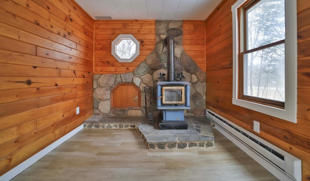 unfurnished living room with a wood stove, a baseboard heating unit, wood walls, and a wealth of natural light