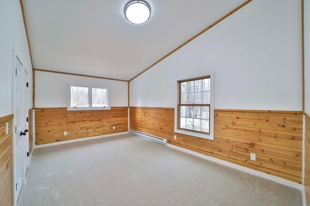 empty room featuring wainscoting, wooden walls, a baseboard radiator, carpet, and vaulted ceiling