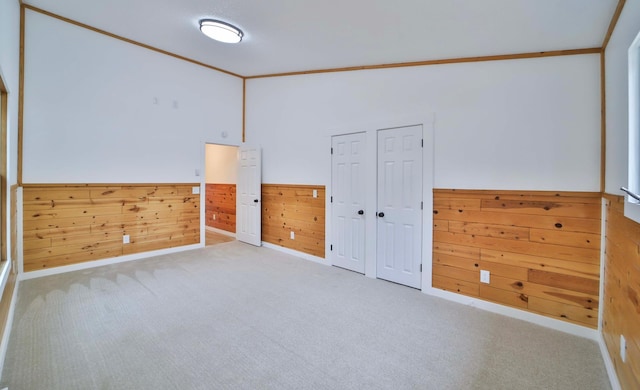 spare room featuring wooden walls, carpet flooring, crown molding, and a wainscoted wall