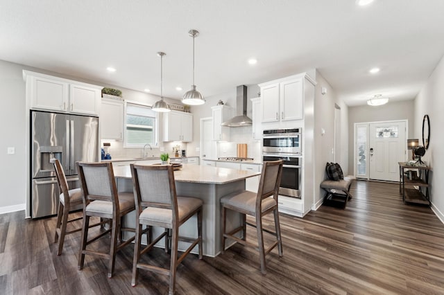 kitchen with a sink, white cabinets, appliances with stainless steel finishes, wall chimney range hood, and a center island