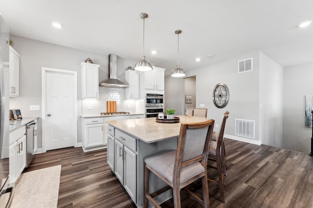 kitchen featuring a breakfast bar, wall chimney range hood, visible vents, and appliances with stainless steel finishes