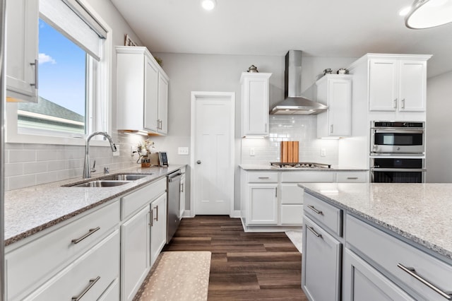 kitchen featuring wall chimney range hood, dark wood-style floors, white cabinets, stainless steel appliances, and a sink