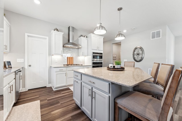 kitchen featuring visible vents, a breakfast bar, dark wood-style flooring, appliances with stainless steel finishes, and wall chimney exhaust hood