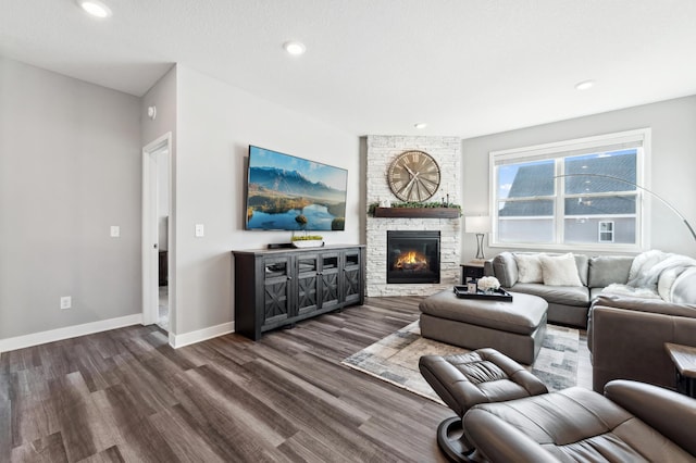 living area featuring a stone fireplace, recessed lighting, baseboards, and dark wood-style flooring