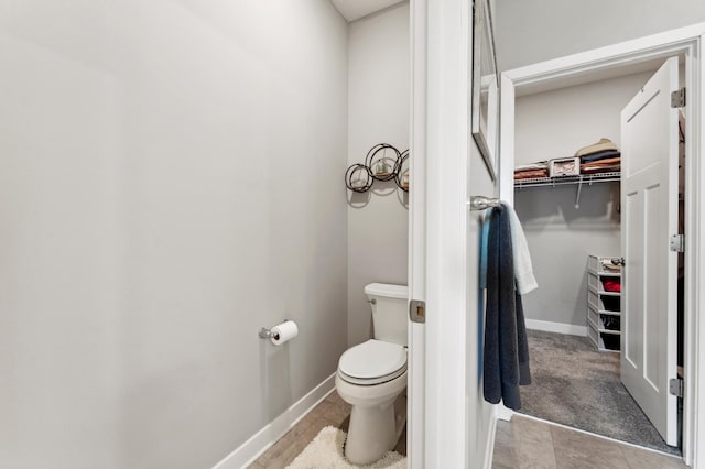 bathroom with baseboards, toilet, and a spacious closet