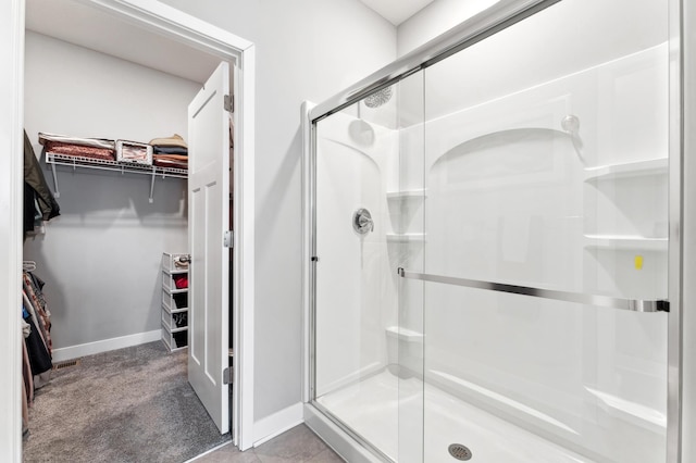 full bath with a spacious closet, a shower stall, and baseboards