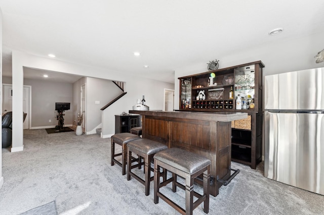 bar with stairs, a dry bar, light colored carpet, and freestanding refrigerator