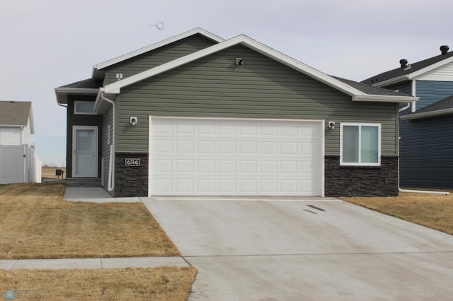 ranch-style home featuring concrete driveway, an attached garage, fence, and stone siding