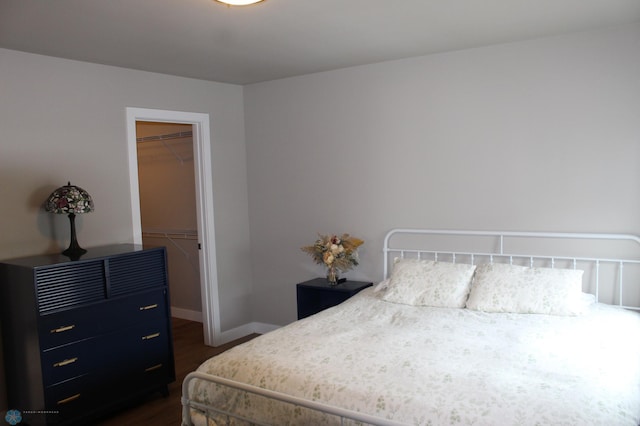 bedroom with a walk in closet, baseboards, a closet, and dark wood-style floors