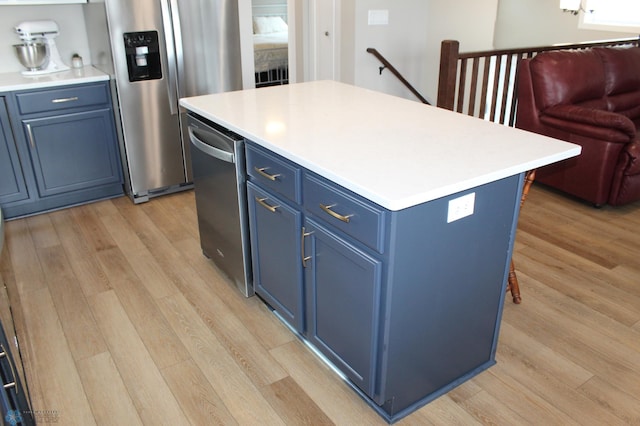 kitchen featuring blue cabinetry, light countertops, a center island, and light wood finished floors