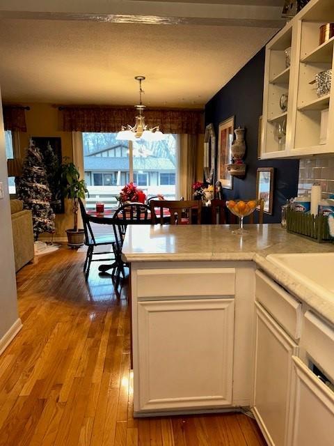 kitchen with wood finished floors, a peninsula, white cabinets, light countertops, and a chandelier