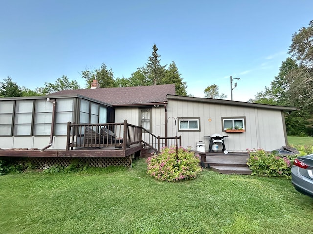 rear view of house featuring a wooden deck, a lawn, and roof with shingles