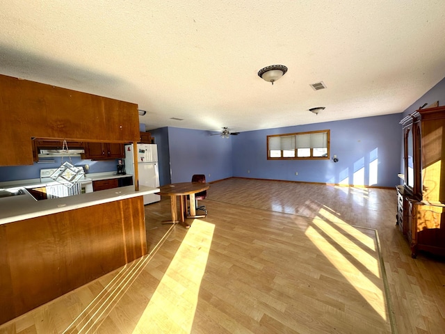 kitchen with visible vents, light countertops, light wood-type flooring, brown cabinets, and freestanding refrigerator