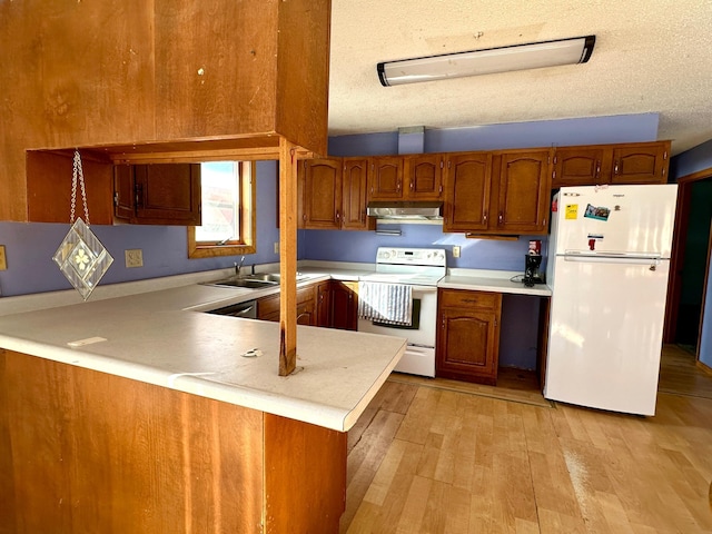 kitchen featuring under cabinet range hood, white appliances, a peninsula, and brown cabinetry