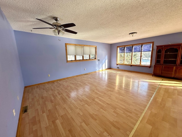 empty room with visible vents, light wood-style flooring, baseboards, and ceiling fan