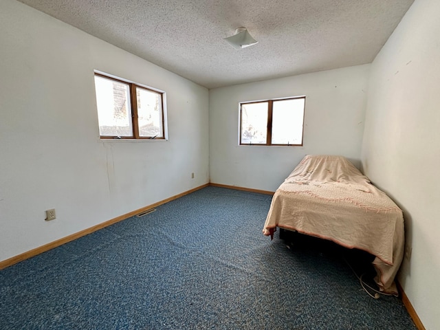 unfurnished bedroom featuring visible vents, baseboards, a textured ceiling, and carpet flooring