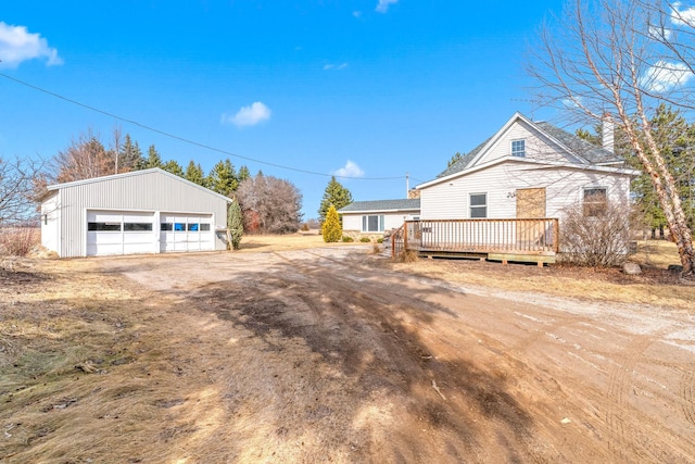 view of side of home featuring a wooden deck, a detached garage, and an outbuilding