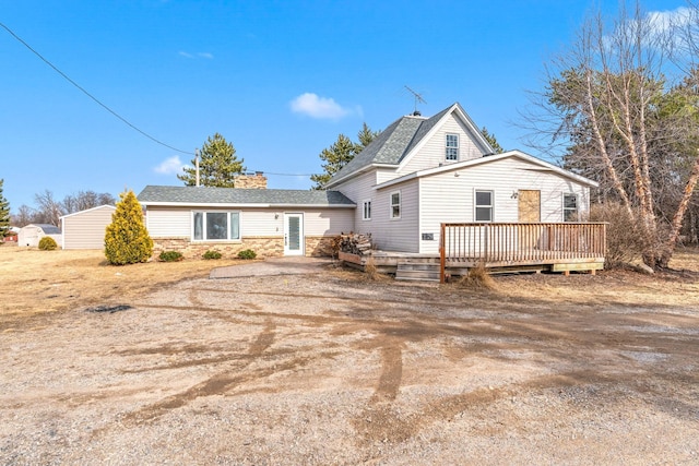 view of front facade featuring stone siding, dirt driveway, a deck, and a chimney