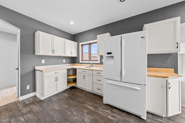 kitchen featuring a sink, white refrigerator with ice dispenser, white cabinets, and light countertops