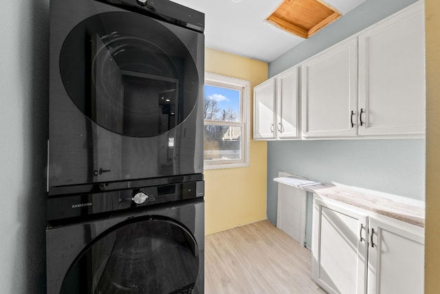 washroom with light wood finished floors, cabinet space, and stacked washing maching and dryer