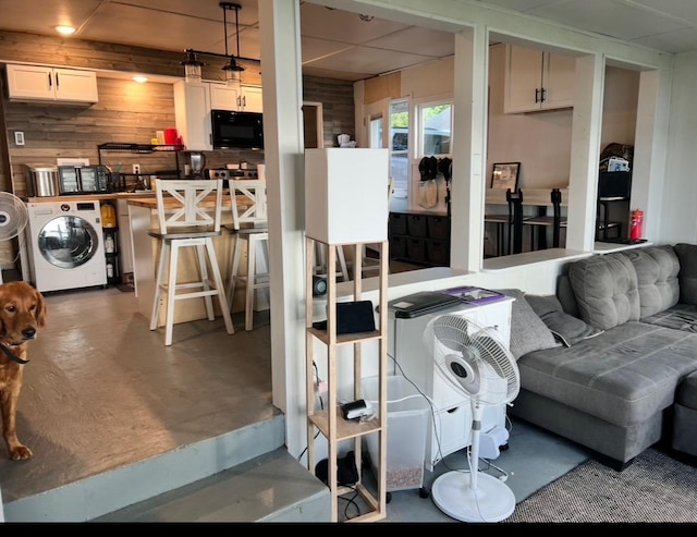 living room with wooden walls, washer / clothes dryer, a drop ceiling, and finished concrete floors