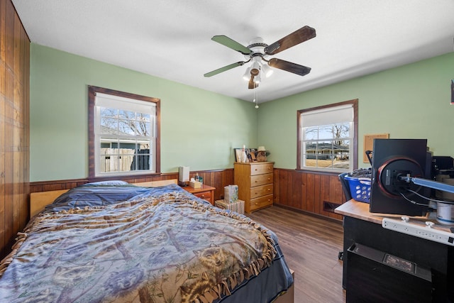 bedroom with a wainscoted wall, wood walls, ceiling fan, and wood finished floors