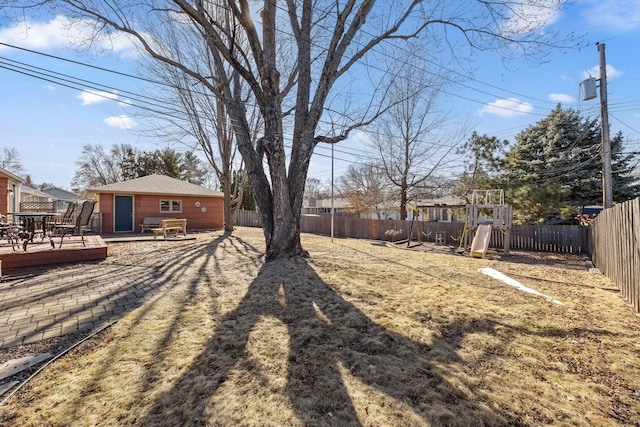 view of yard with a deck, outdoor dining space, a playground, and a fenced backyard