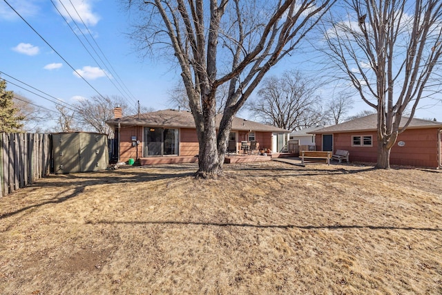 back of property with fence, a wooden deck, a chimney, an outdoor structure, and a storage unit