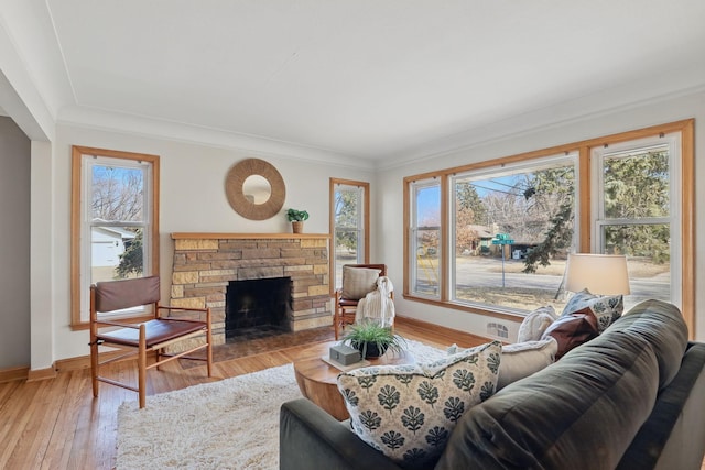 living room with visible vents, crown molding, baseboards, a stone fireplace, and light wood-style floors