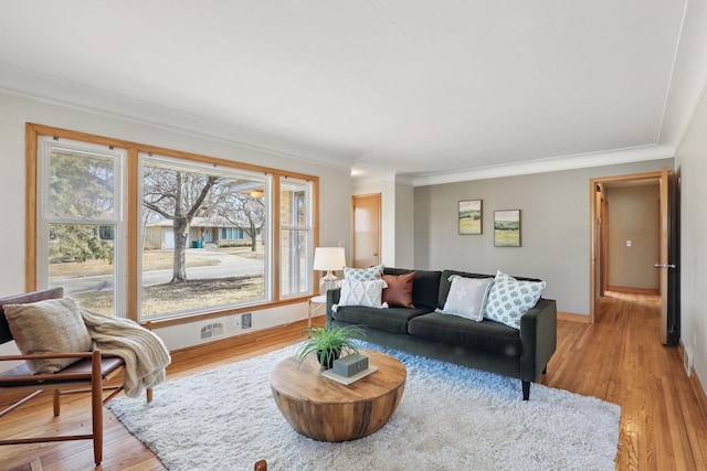 living area featuring a healthy amount of sunlight, ornamental molding, and light wood finished floors