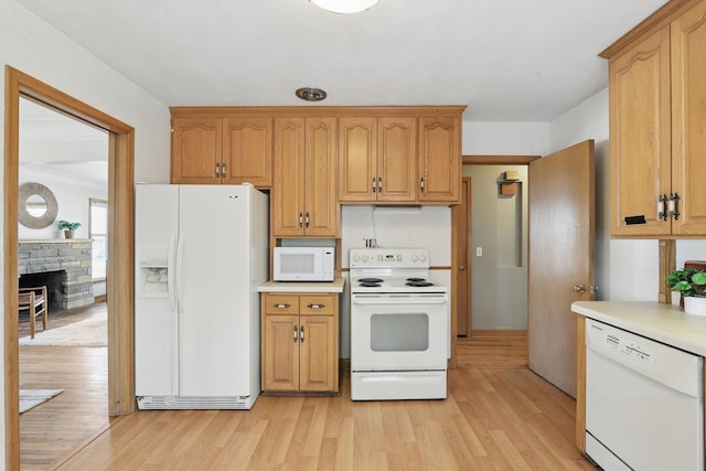 kitchen with light wood-type flooring, white appliances, a stone fireplace, and light countertops