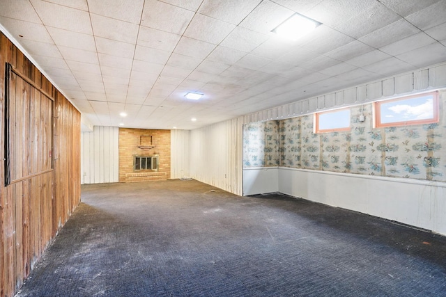 basement featuring wooden walls, a fireplace, carpet floors, and wainscoting