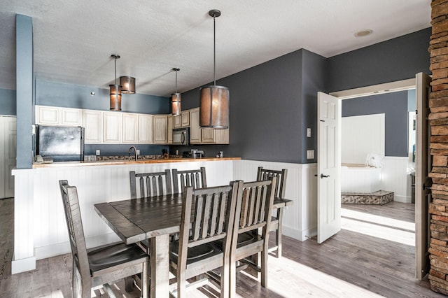 dining space with a textured ceiling, light wood-style flooring, and wainscoting