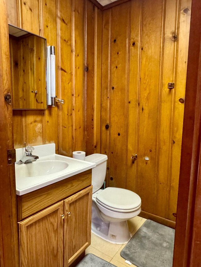 half bath with tile patterned flooring, wooden walls, vanity, and toilet