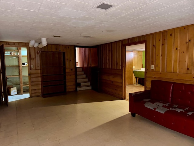 unfurnished living room with stairs, tile patterned floors, wooden walls, and visible vents