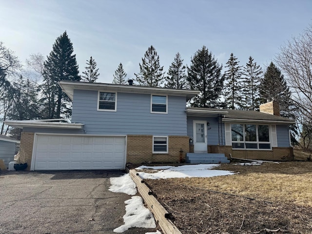 tri-level home with brick siding, a chimney, aphalt driveway, and a garage