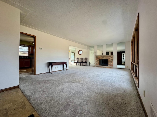 unfurnished living room featuring visible vents, a textured ceiling, carpet floors, a stone fireplace, and baseboards