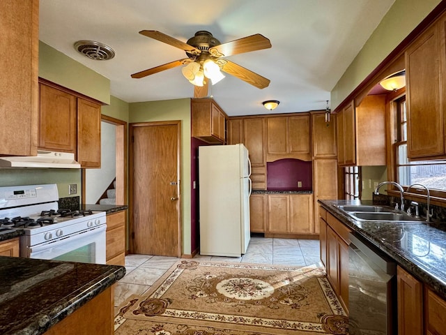 kitchen featuring white appliances, dark stone countertops, visible vents, a sink, and under cabinet range hood