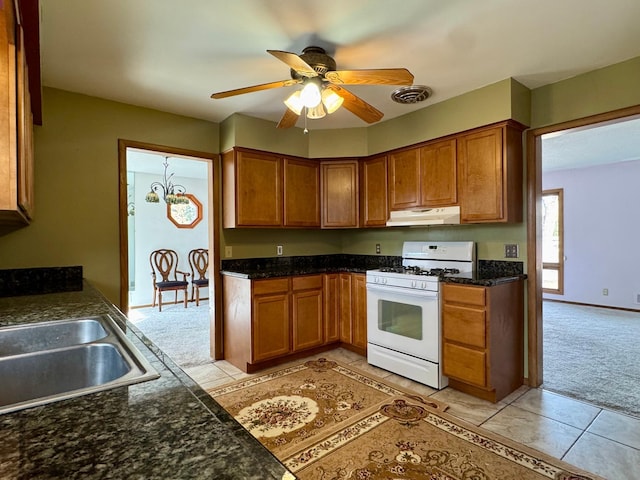 kitchen with visible vents, white gas stove, under cabinet range hood, light colored carpet, and brown cabinets