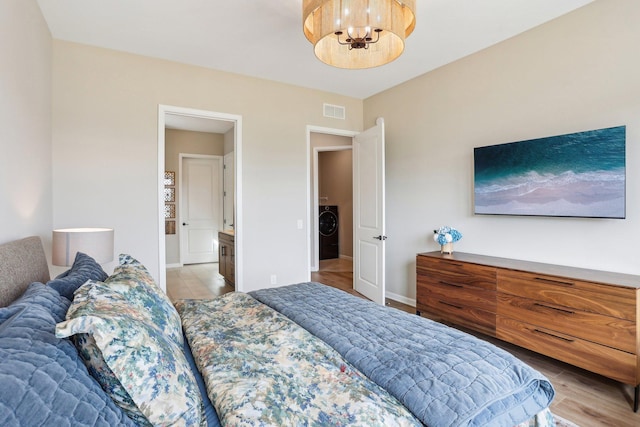 bedroom with visible vents, baseboards, an inviting chandelier, light wood-style flooring, and washer / dryer