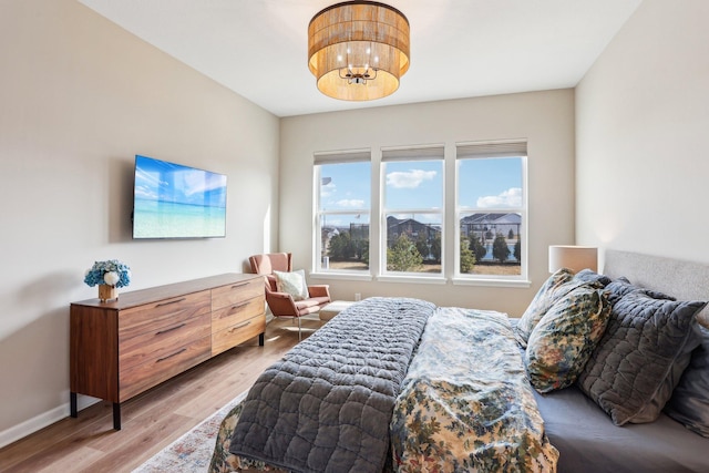 bedroom featuring light wood-type flooring, an inviting chandelier, and baseboards