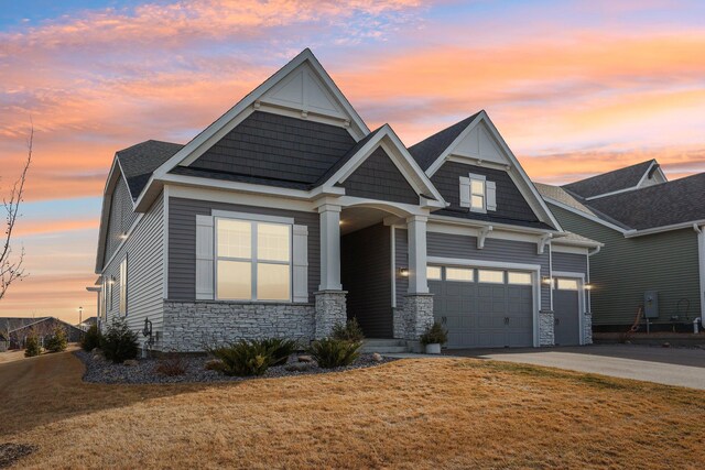craftsman-style home with an attached garage, driveway, stone siding, and a front lawn