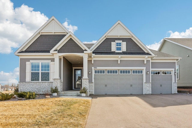 craftsman inspired home with a front yard, an attached garage, stone siding, and driveway