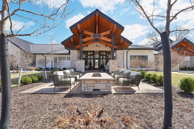 rear view of house featuring a patio, stone siding, an outdoor living space with a fire pit, a standing seam roof, and metal roof