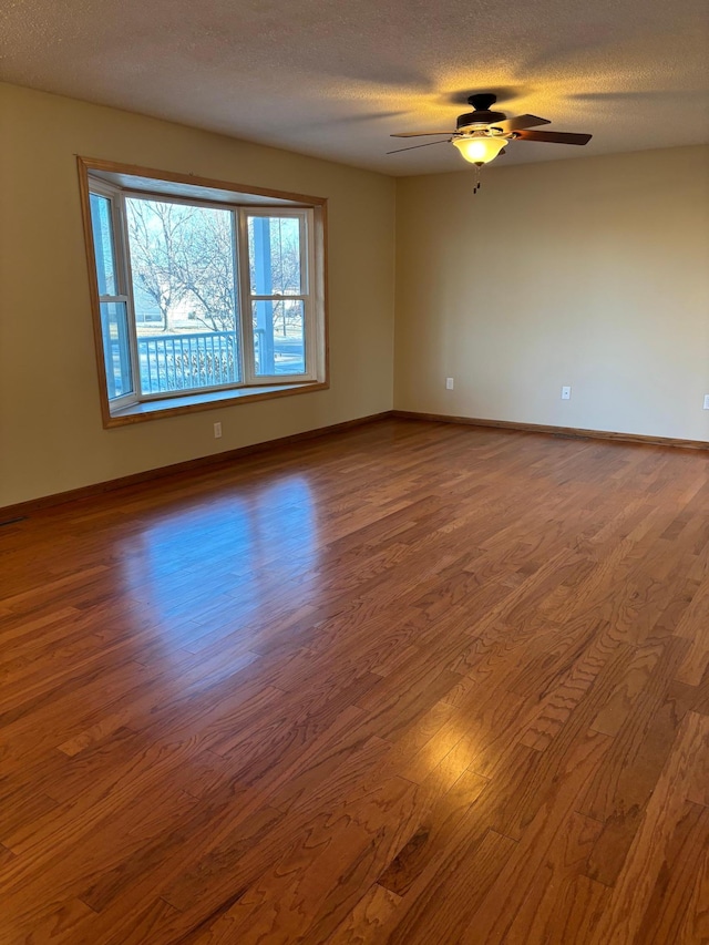 spare room featuring baseboards, a textured ceiling, wood finished floors, and a ceiling fan